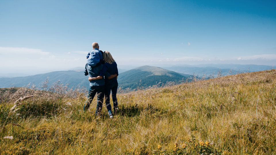 Couple standing on hill top looking at mountains in the distance 