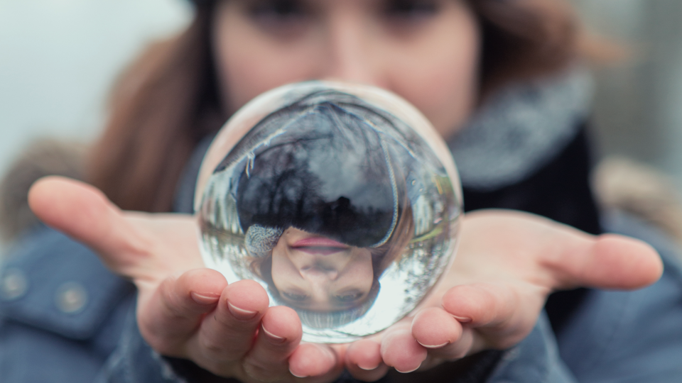 Blurred image of woman inthe background holding a glass ball in the foreground that focuses her image and inverts it 