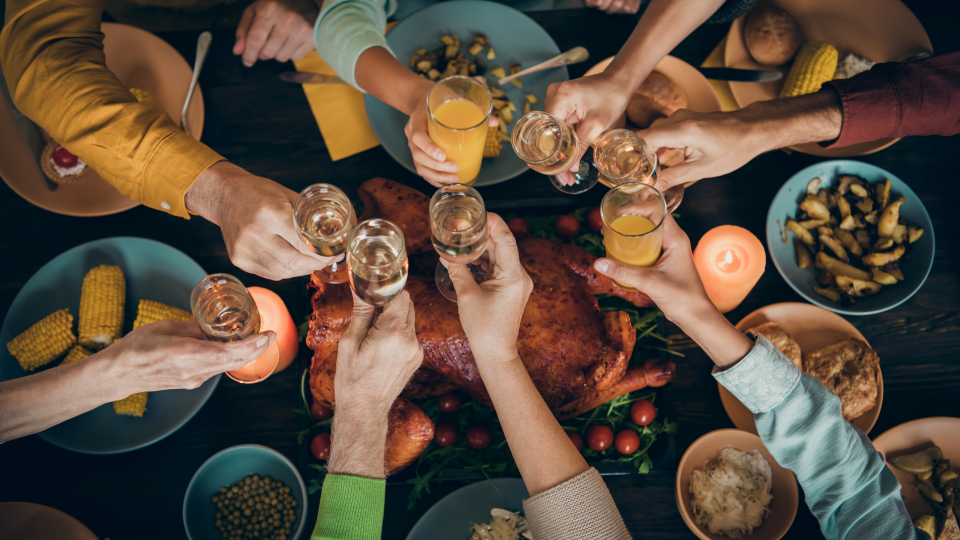 Top down view of dinner table with eight people's arms toasting with drinks over the table