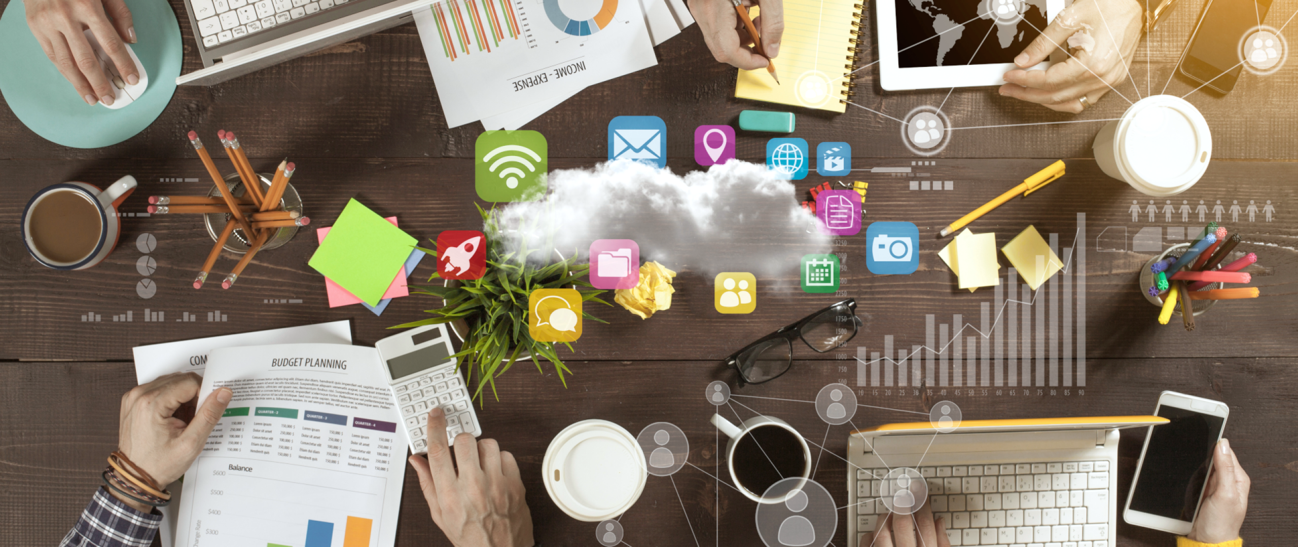 Top down view of table with laptops, tablets and reports with various business icons in the center