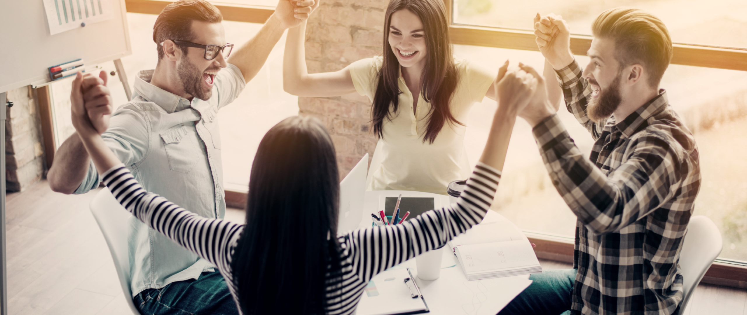 Four people sitting around a table with their arm raised in celebration holding hands