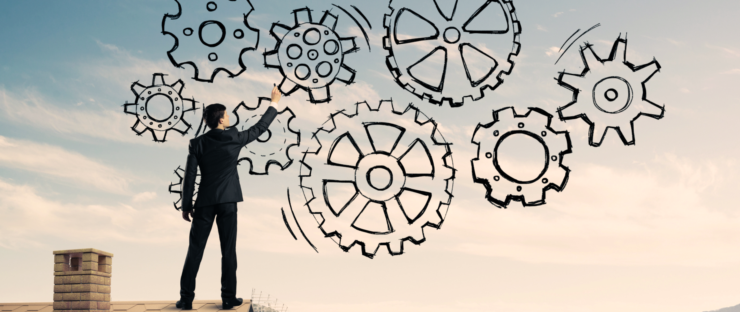 Business man standing on rooftop with hand drawn interconnected gears in the sky