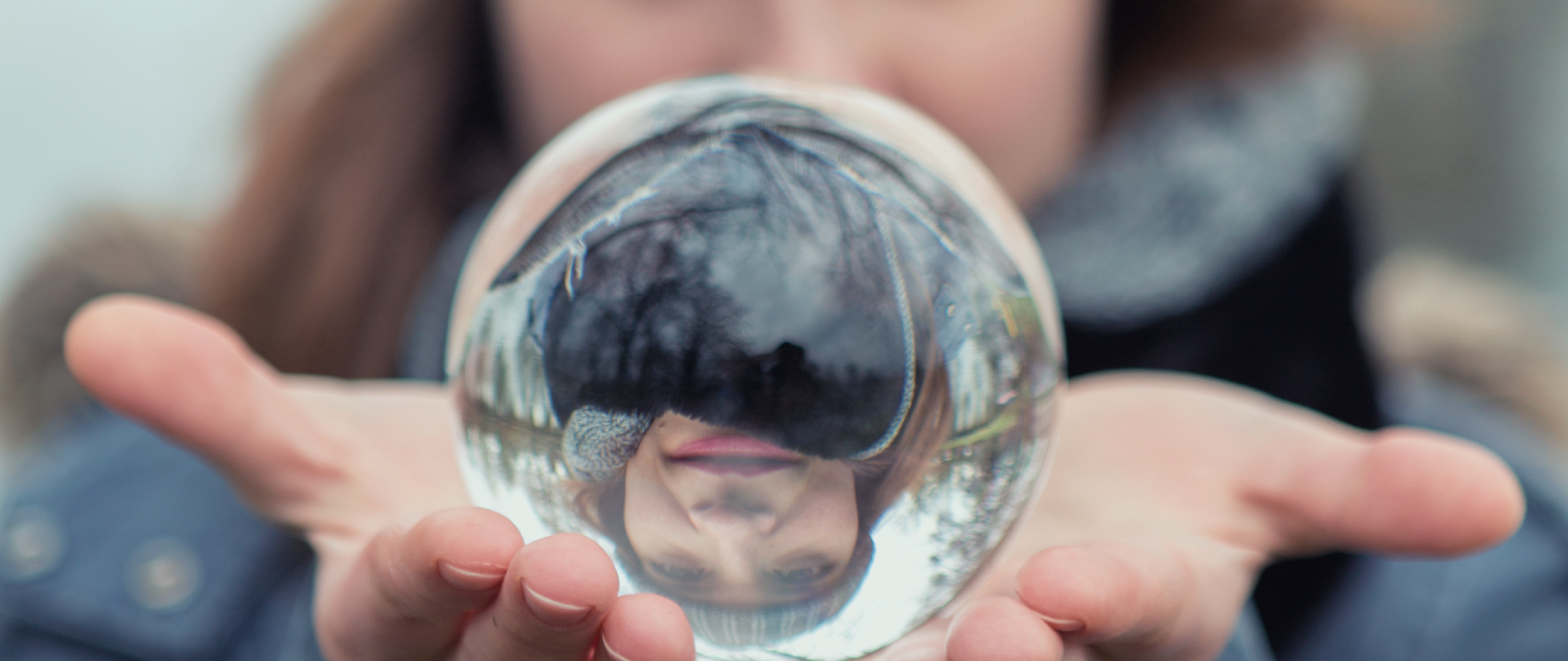 Blurred image of woman inthe background holding a glass ball in the foreground that focuses her image and inverts it 