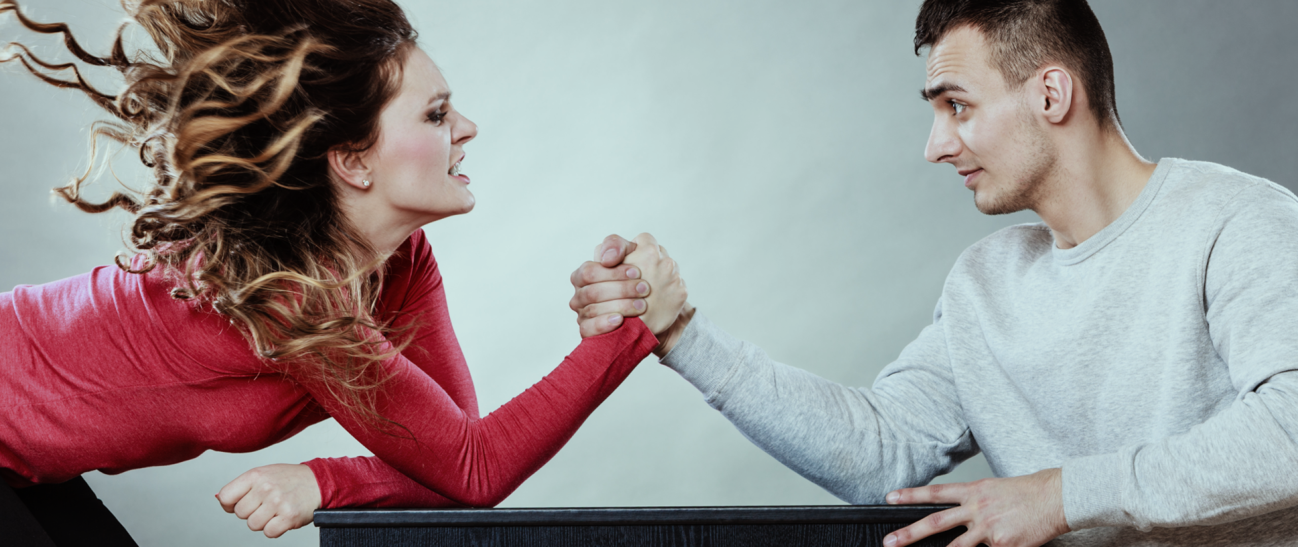Woman in fiery red top and wild hair arm wrestling  