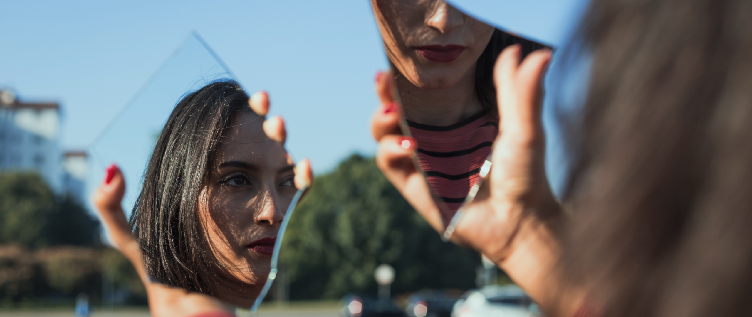 Woman's hands holding two broken mirror pieces which are reflecting two parts of her face at different angles 