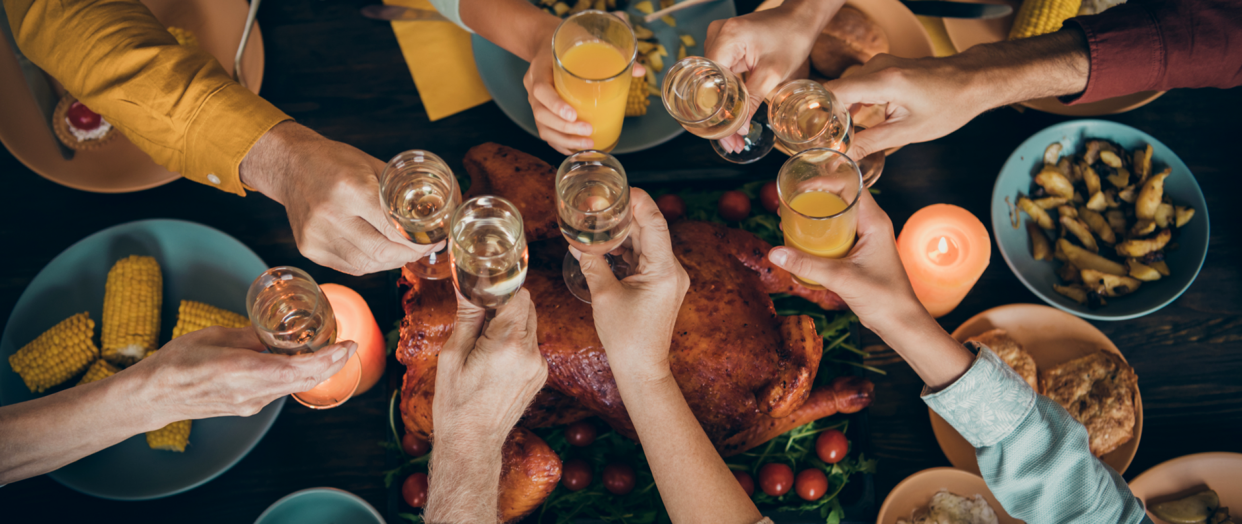 Top down view of dinner table with eight people's arms toasting with drinks over the table